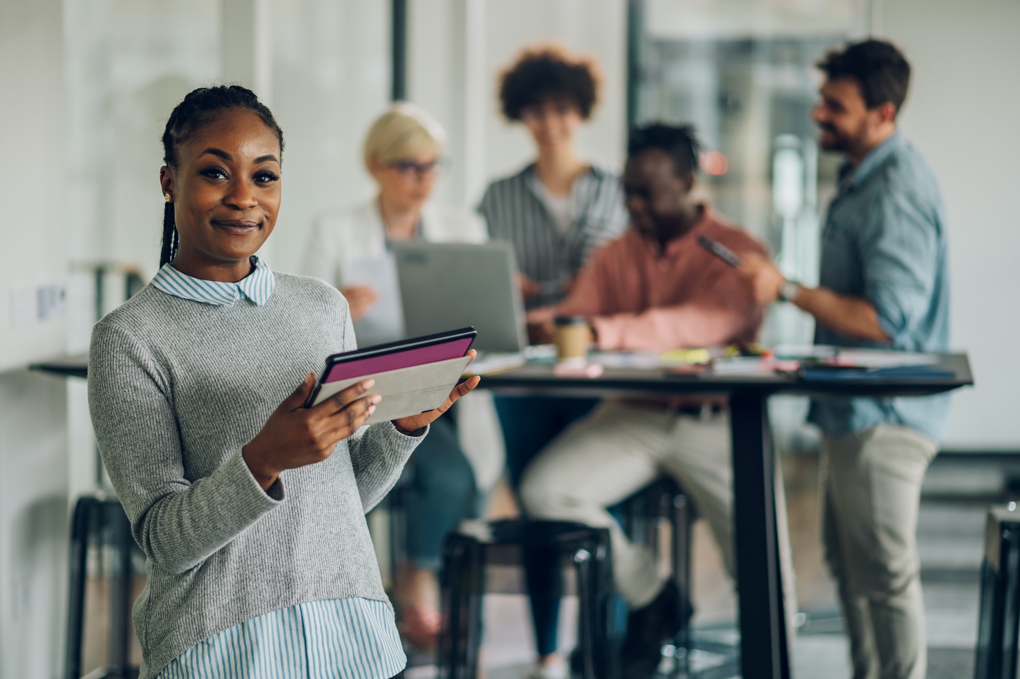 African american business woman standing in a office with colleagues in the back